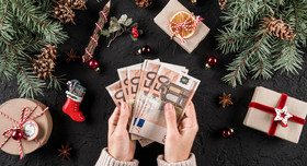 Zwei Hände halten mehrere 50-Euroscheine fest, drumherum ist weihnachtliche Deko zu sehen. Foto: Jukov studio - stock.adobe.com
