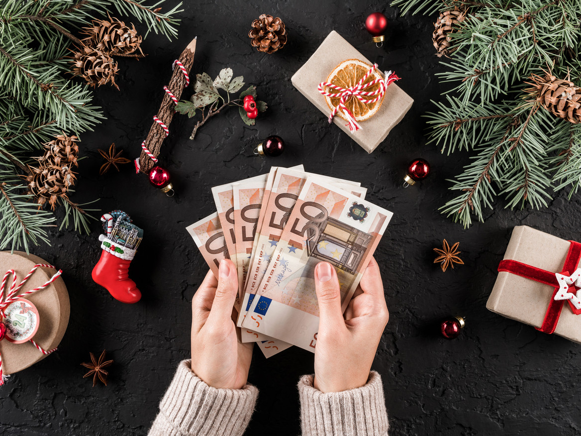 Zwei Hände halten mehrere 50-Euroscheine fest, drumherum ist weihnachtliche Deko zu sehen. Foto: Jukov studio - stock.adobe.com