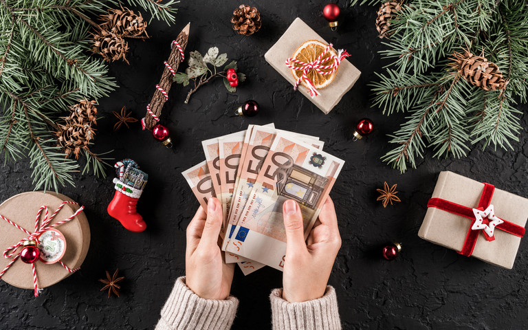 Zwei Hände halten mehrere 50-Euroscheine fest, drumherum ist weihnachtliche Deko zu sehen. Foto: Jukov studio - stock.adobe.com