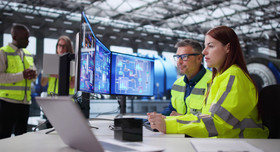 Ein konzentriertes Fachkräfteteam beobachtet an mehreren Monitoren die Produktionsprozesse eines Industrieunternehmens.