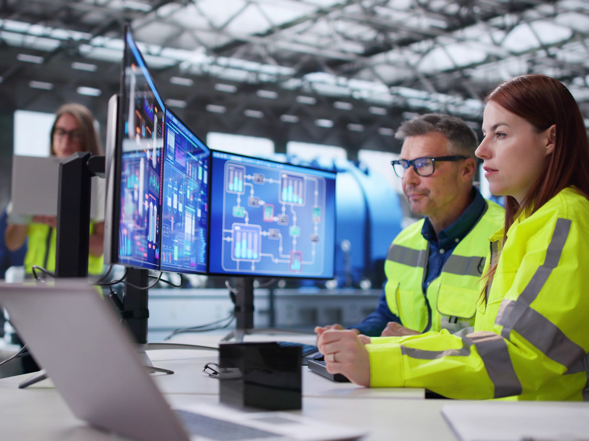 Ein konzentriertes Fachkräfteteam beobachtet an mehreren Monitoren die Produktionsprozesse eines Industrieunternehmens.
