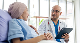 Ein empathischer Arzt mit Stethoskop und Tablet besucht eine junge Krebspatientin am Krankenbett.