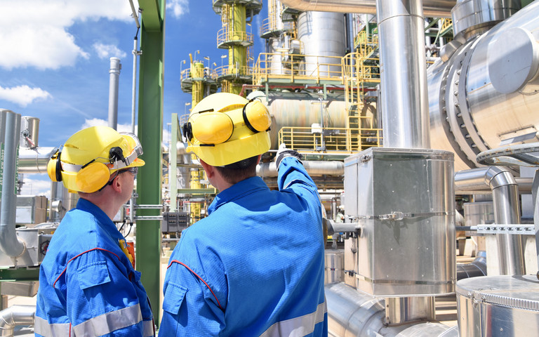 Zwei Beschäftigte mit Schutzhelmen unterhalten sich auf dem Gelände einer Chemiefabrik. 
