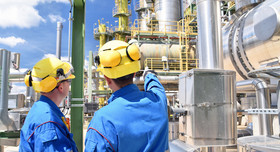 Zwei Beschäftigte mit Schutzhelmen unterhalten sich auf dem Gelände einer Chemiefabrik. 
