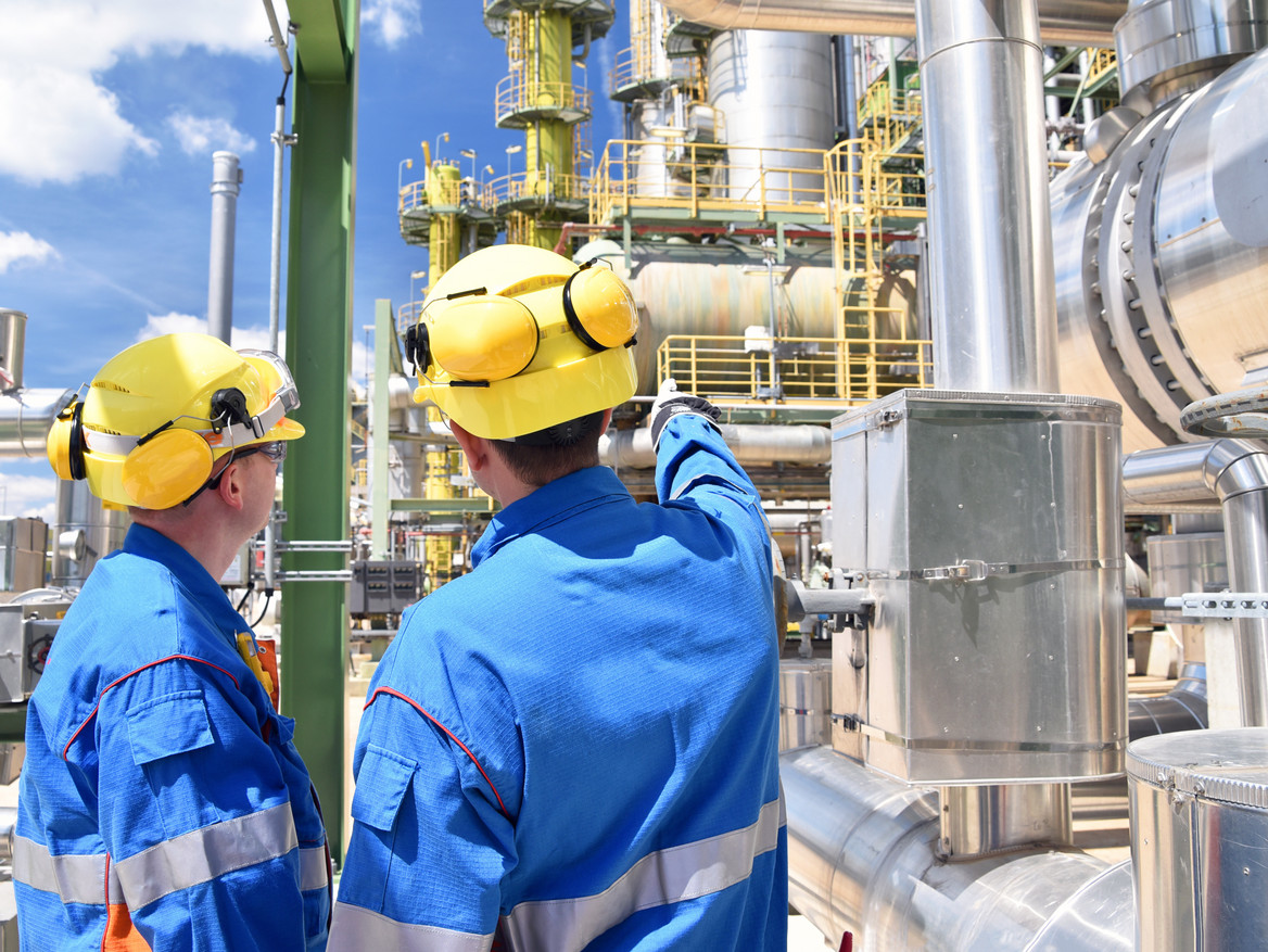 Zwei Beschäftigte mit Schutzhelmen unterhalten sich auf dem Gelände einer Chemiefabrik. 