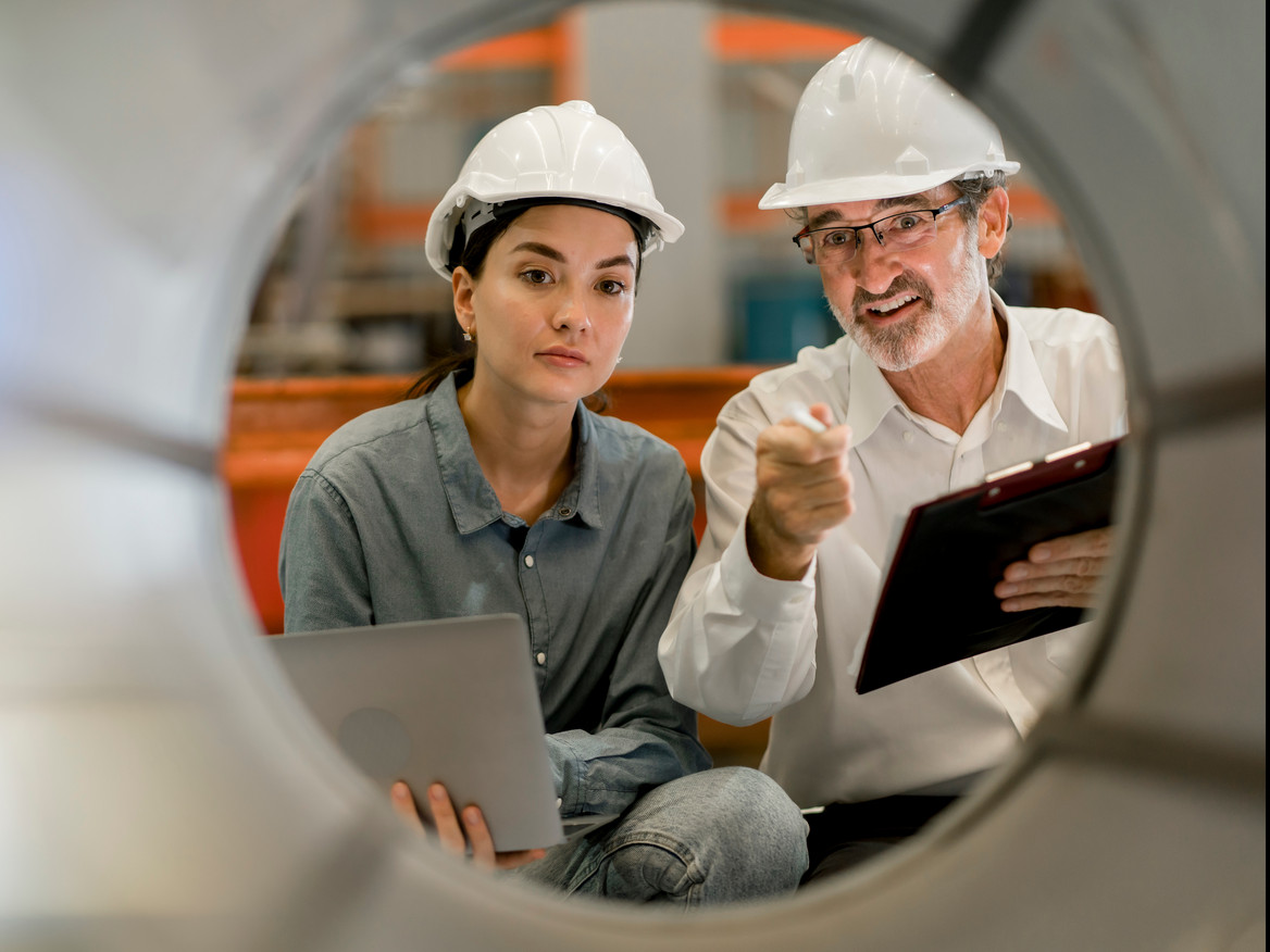 Eine junge Ingenieurin und ein älterer Kollege bei der Prüfung von Industrieanlagen.