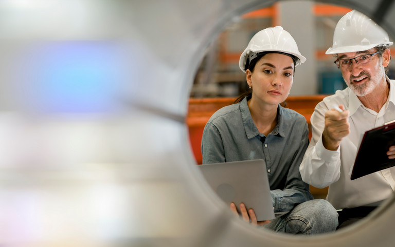 Eine junge Ingenieurin und ein älterer Kollege bei der Prüfung von Industrieanlagen.