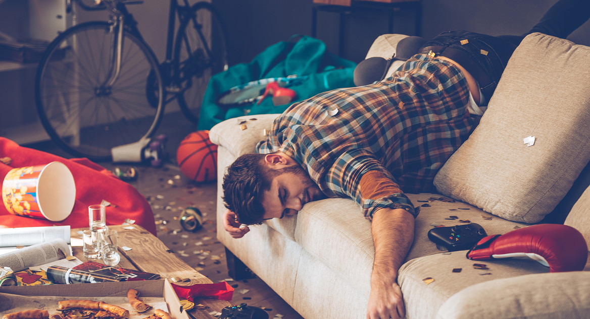 Junger Mann hängt nach einer Party kopfüber auf seinem Sofa.