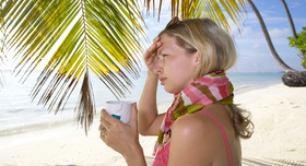 Eine Urlauberin am Strand mit Schal und einer Tasse Tee. 