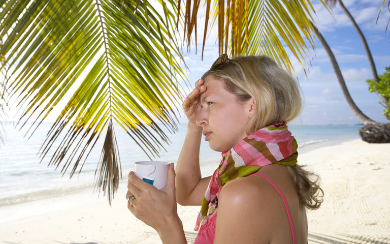 Eine Urlauberin am Strand mit Schal und einer Tasse Tee. 