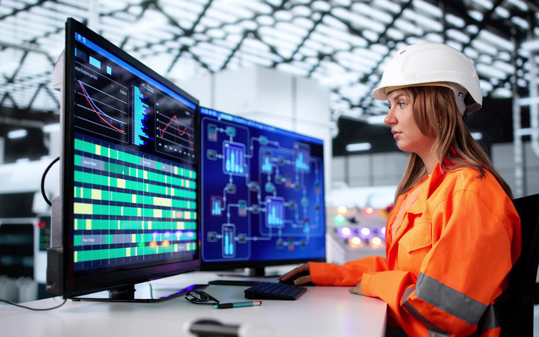 Ingenieurin beobachtet konzentriert an mehreren Monitoren die Steuerung eines Produktionsprozesses.