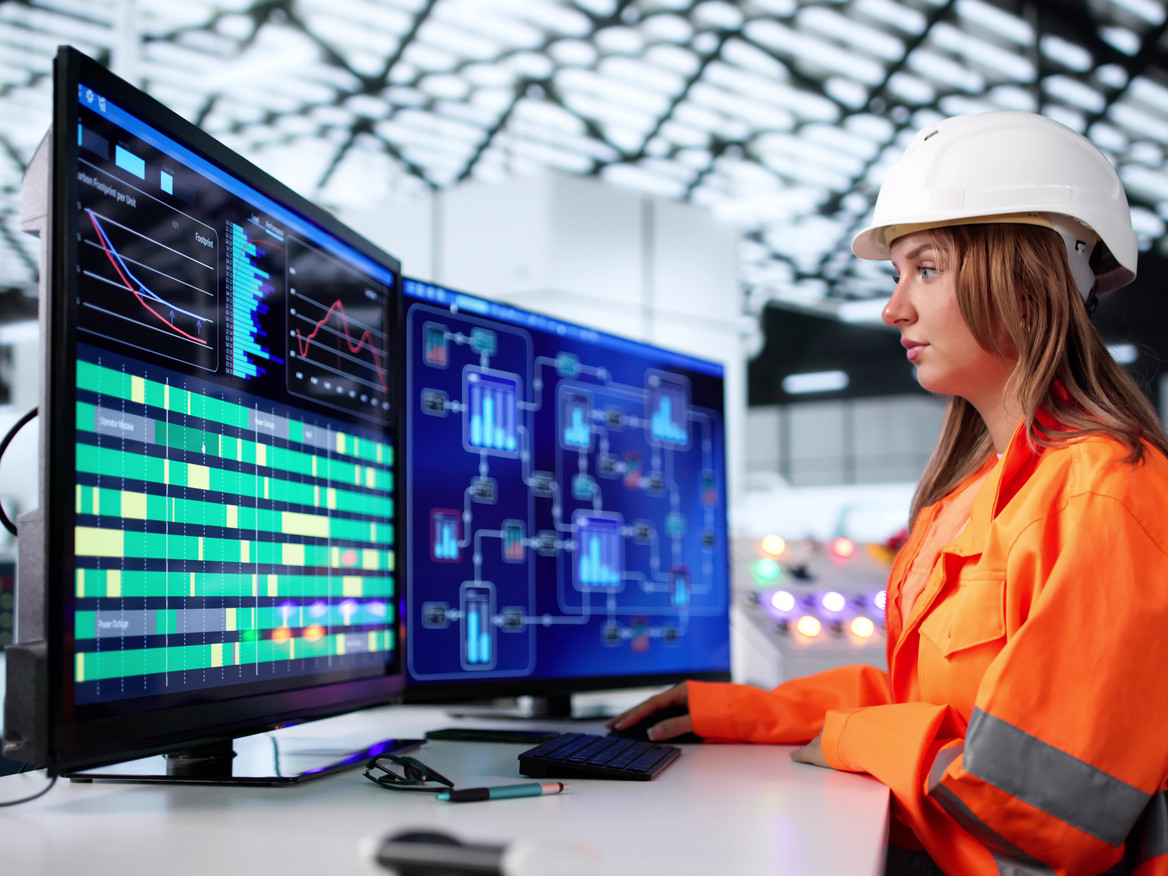 Ingenieurin beobachtet konzentriert an mehreren Monitoren die Steuerung eines Produktionsprozesses.