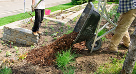 Zwei männliche Personen mit Laubgabel und Schubkarre bei der Gartenarbeit im Frühling.