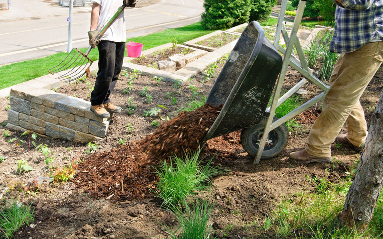 Zwei männliche Personen mit Laubgabel und Schubkarre bei der Gartenarbeit im Frühling.