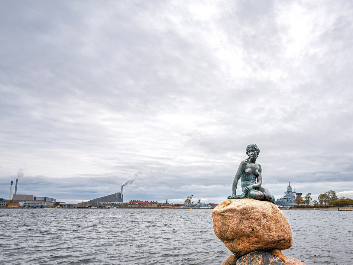 Skulptur der kleinen Meerjungfrau vor der Küste und Skyline Kopenhagens.
