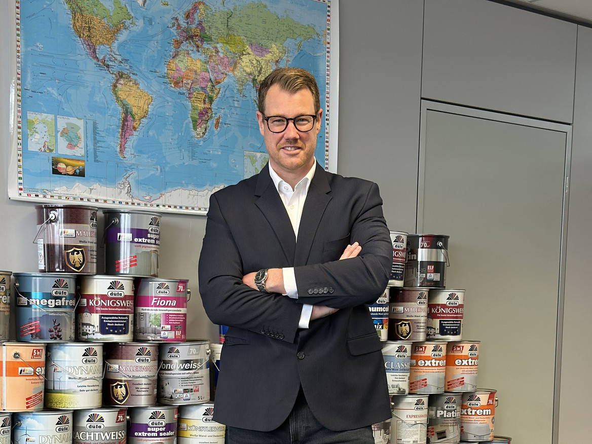 Christian Starke steht vor einer Weltkarte, im Hintergrund Meffert-Produkte. 