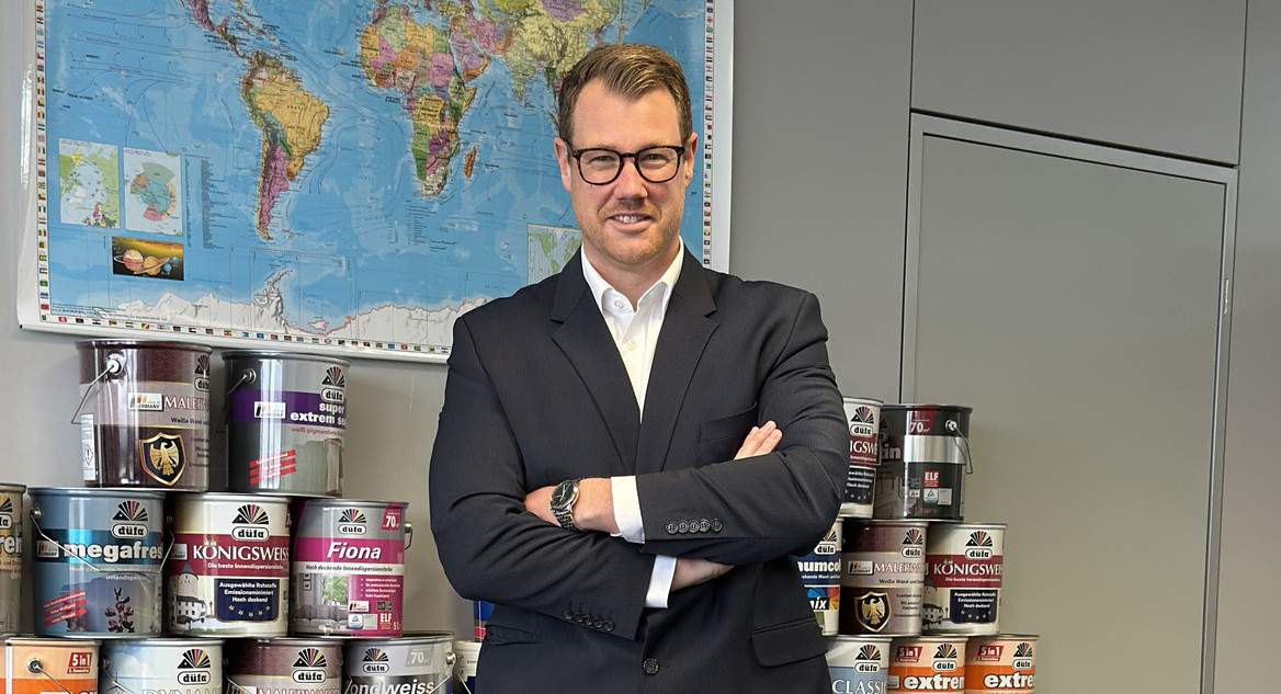 Christian Starke steht vor einer Weltkarte, im Hintergrund Meffert-Produkte. 