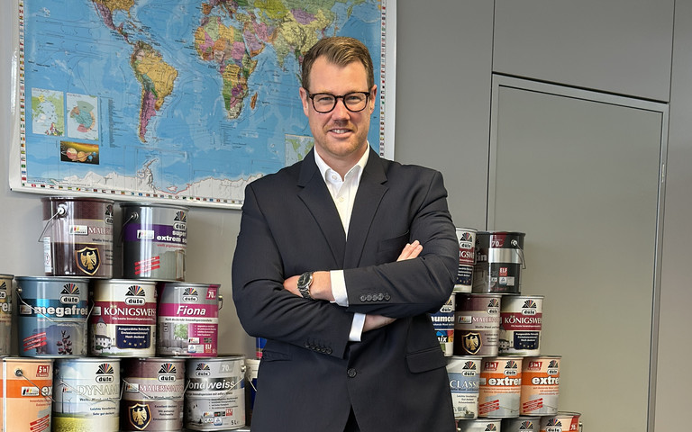 Christian Starke steht vor einer Weltkarte, im Hintergrund Meffert-Produkte. 