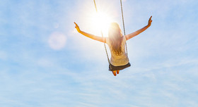 Frau auf einer Schaukel mit blauem Himmel im Gegenlicht