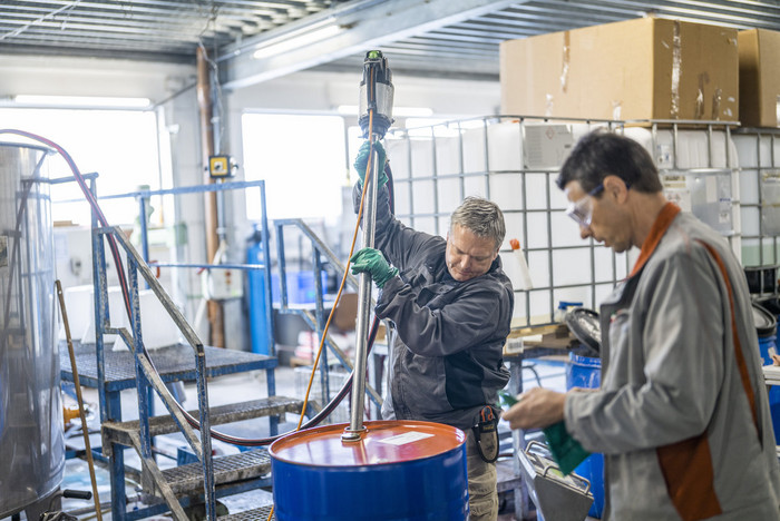 Zwei Männer mischen Reinigungsmittel in einem Metallfass