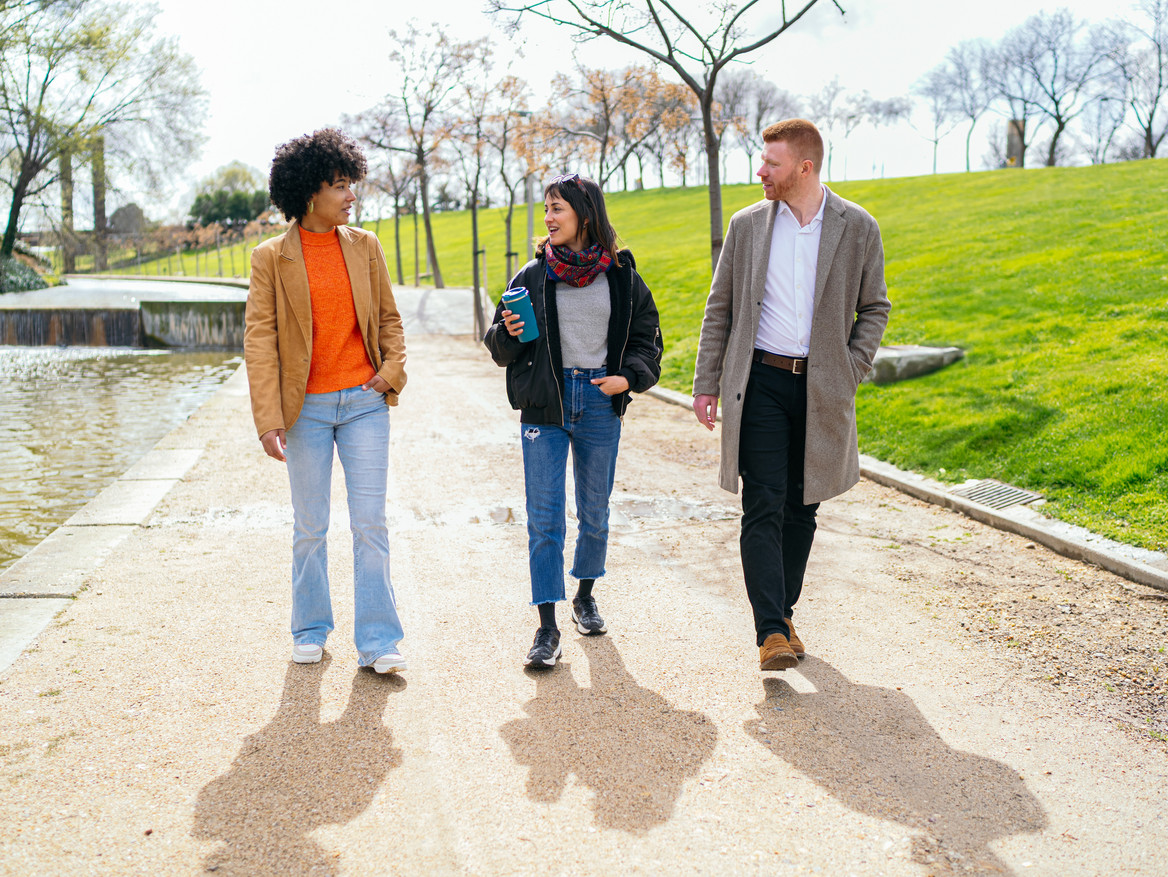 Drei Arbeitskollegen spazieren in der Pause durch einen sonnigen Park.