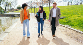 Drei Arbeitskollegen spazieren in der Pause durch einen sonnigen Park.