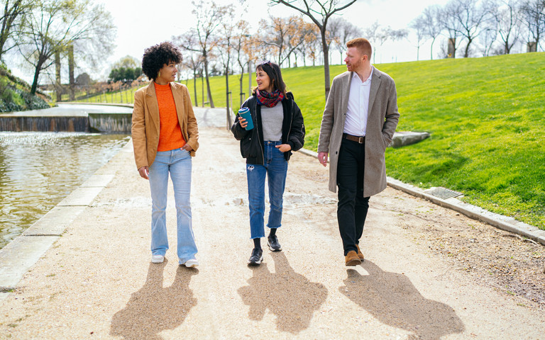 Drei Arbeitskollegen spazieren in der Pause durch einen sonnigen Park.