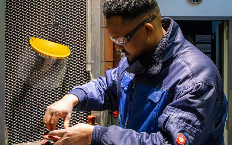 Regan Kifle Negash arbeitet mit Schutzbrille und Arbeitsjacke an einer Maschine.
