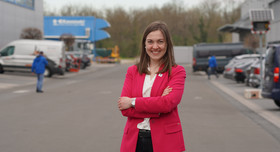 Clara Scherner steht auf dem Werksgelände, trägt Businesskleidung und schaut lächelnd in die Kamera.