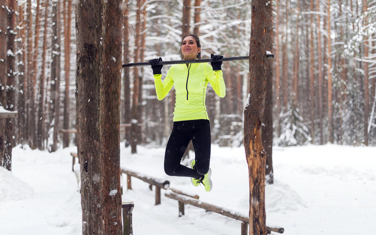 Eine Frau macht Fitnessübungen an einer Anlage im Wald.