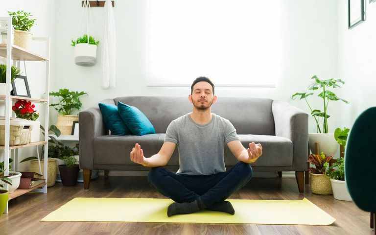 Ein Mann meditiert im Wohnzimmer.