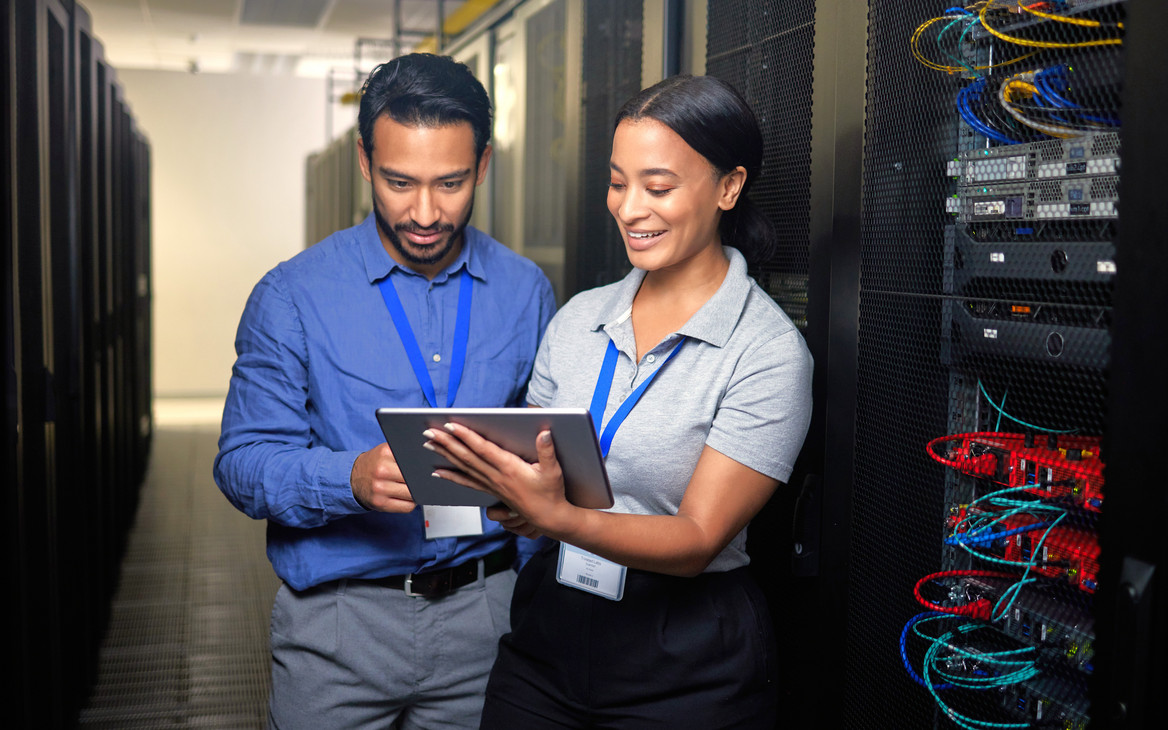 Eine IT-Sicherheitskoordinatorin mit Tablet und ihr Kollege beim Cybersecurity-Check im Serverraum.