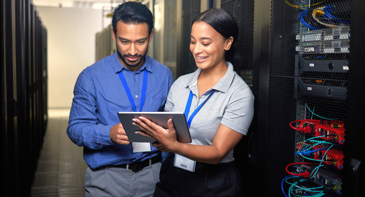 Eine IT-Sicherheitskoordinatorin mit Tablet und ihr Kollege beim Cybersecurity-Check im Serverraum.