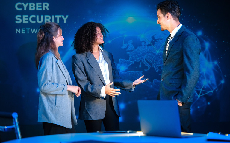 Dreiköpfiges Cybersecurity-Team unterhält sich stehend angeregt in einem Meetingraum.