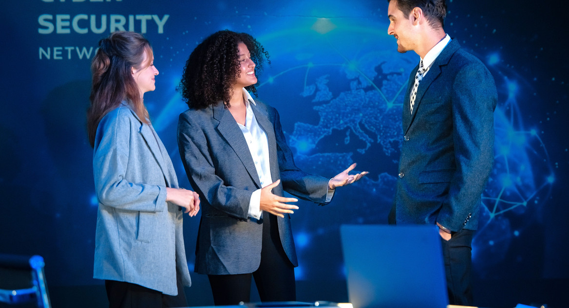 Dreiköpfiges Cybersecurity-Team unterhält sich stehend angeregt in einem Meetingraum.