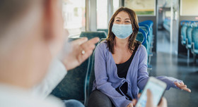 Zwei Reisende mit Maske unterhalten sich in einem Zug.