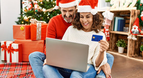 Ein Paar checkt erfreut den Kontostand unterm Weihnachtsbaum: Die Jahressonderzahlung ist eingetroffen.