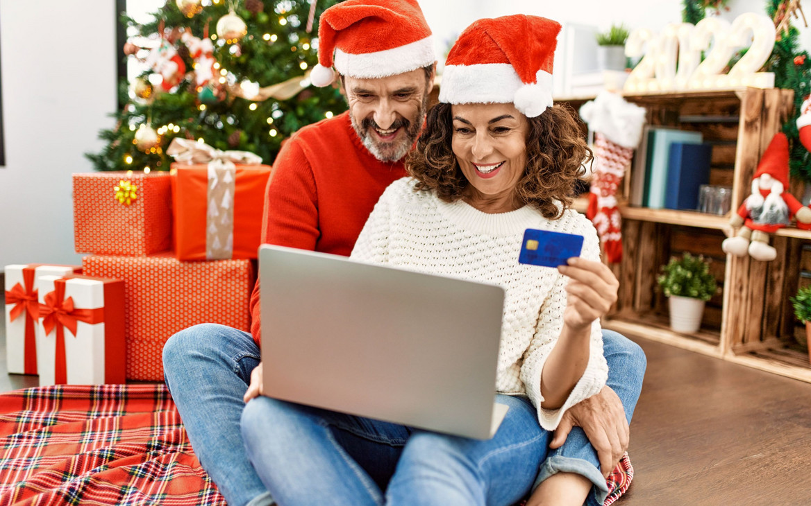 Ein Paar checkt erfreut den Kontostand unterm Weihnachtsbaum: Die Jahressonderzahlung ist eingetroffen.