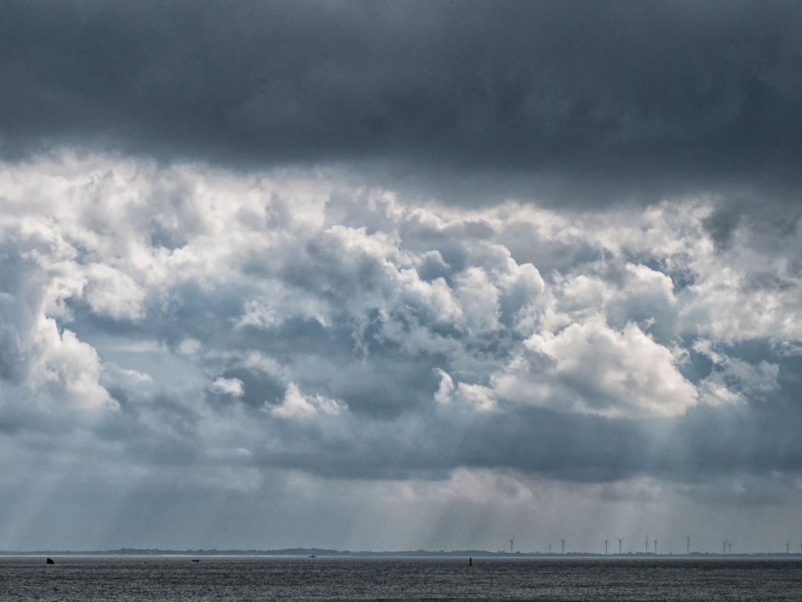 Blick auf die Nordsee, eine Skyline mit Windrädern und einen dramatischen Wolkenhimmel bei Wilhelmshaven.