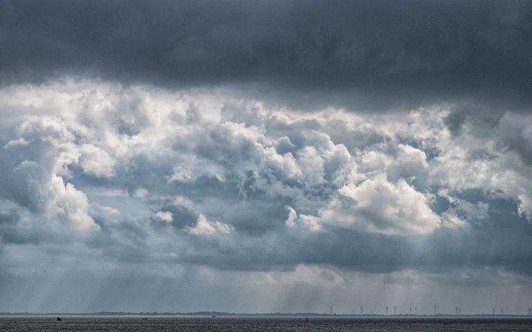 Blick auf die Nordsee, eine Skyline mit Windrädern und einen dramatischen Wolkenhimmel bei Wilhelmshaven.