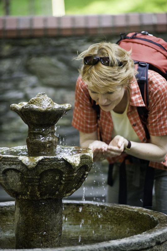 Eine Frau trinkt einen Schluck Wasser am Brunnen. 
