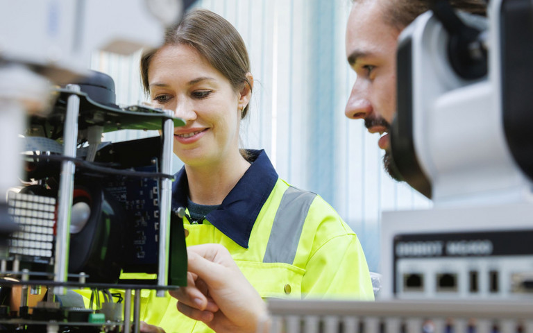 Zwei junge angehende Technikprofis bei der Steuerung von Robotikelementen in einer Lehrwerkstatt.