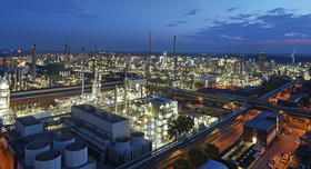 Nächtliche Luftaufnahme des BASF-Verbundstandorts Ludwigshafen: Das weitläufige Industrieareal erstreckt sich bis zum Horizont und ist hell erleuchtet. Zu sehen sind zahlreiche Produktionsanlagen, Türme, Rohrleitungen und Gebäude, durchzogen von beleuchteten Straßen. Im Hintergrund ist der Abendhimmel in Blau- und Rottönen zu erkennen.