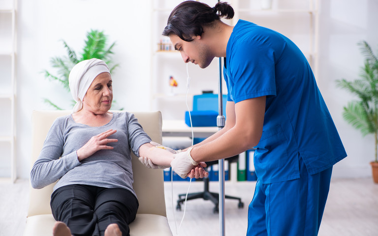 Junger Arzt kümmert sich um eine ältere Krebspatientin.