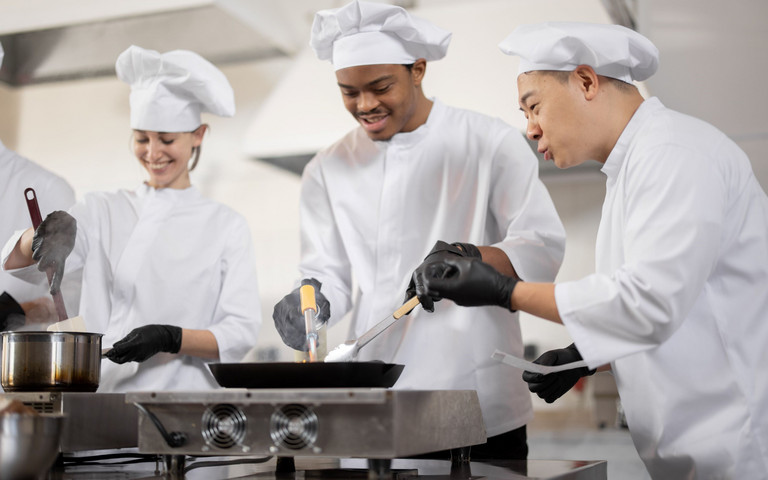 Multikulturelles Kochteam beim Kochen und Braten in einer professionellen Küche.