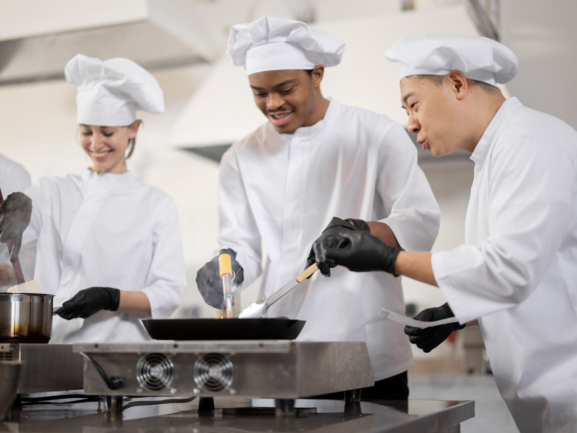 Multikulturelles Kochteam beim Kochen und Braten in einer professionellen Küche.