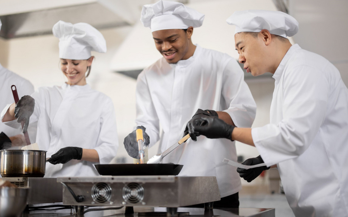 Multikulturelles Kochteam beim Kochen und Braten in einer professionellen Küche.