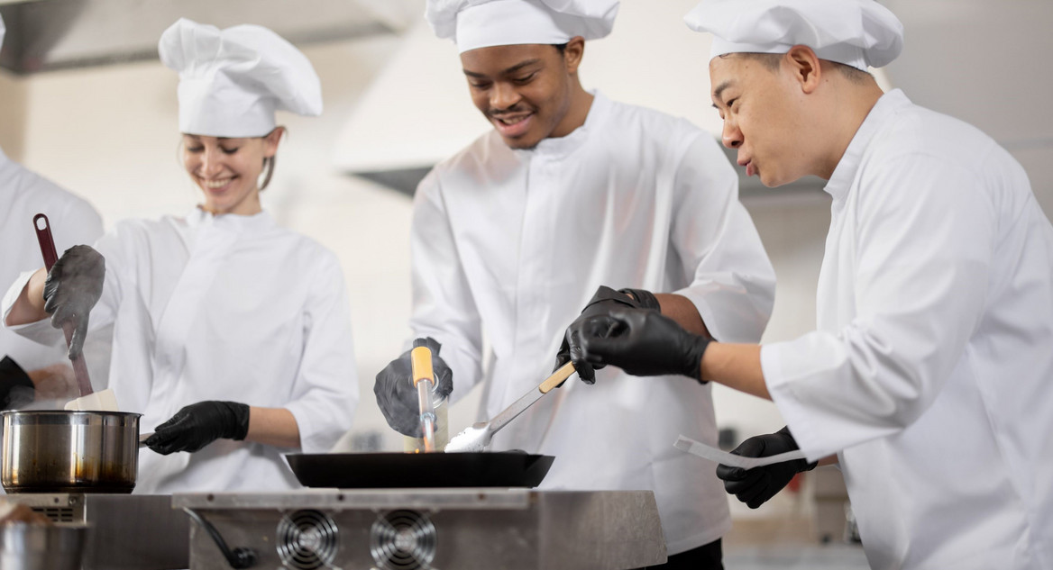 Multikulturelles Kochteam beim Kochen und Braten in einer professionellen Küche.