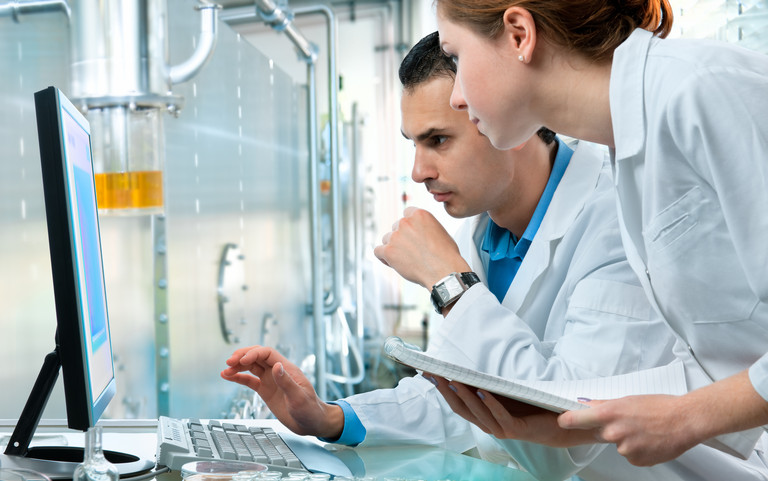 Two chemical industry workers look at a computer monitor.