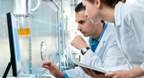 Two chemical industry workers look at a computer monitor.